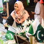 A woman busy in selection and purchasing Pakistan Independence Day related stuff from stall in the city