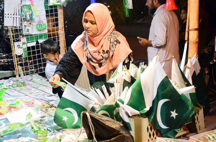 A woman busy in selection and purchasing Pakistan Independence Day related stuff from stall in the city