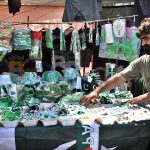 A vendor arranging and displaying national flags and other decorative items related to Independence Day celebrations at his roadside setup