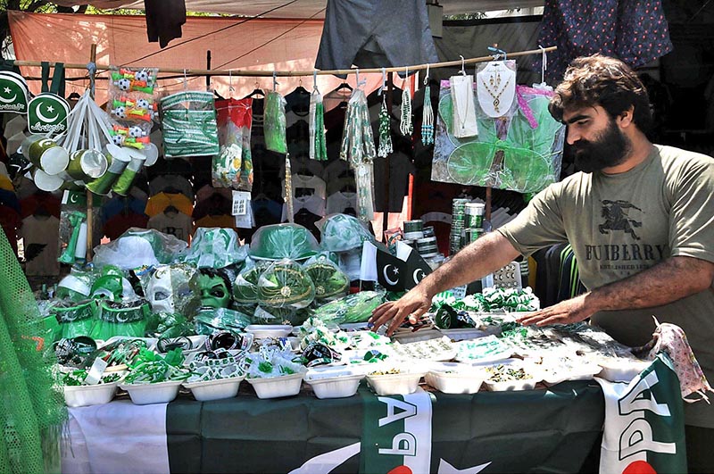 A vendor arranging and displaying national flags and other decorative items related to Independence Day celebrations at his roadside setup