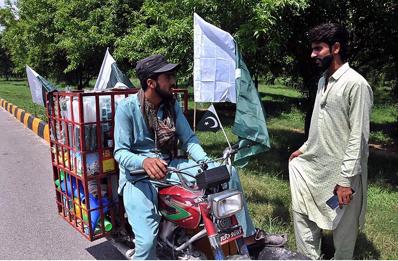A vendor arranging and displaying national flags and other decorative items related to Independence Day celebrations at his roadside setup