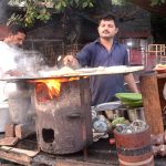 Vendor busy in preparing bread (Paratha) for customer at his roadside setup
