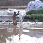 A vendor washing plastic sacks in local canal for reuse