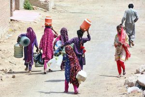 Gypsy girls on the way while carrying water canes for filling clean water at Qasimabad