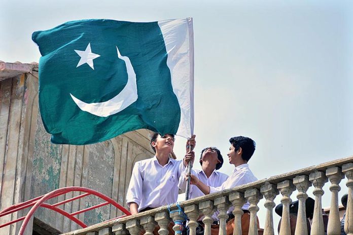 Students install national flag on the roof of private school at Latifabad in connection with Pakistan Independence Day celebrations