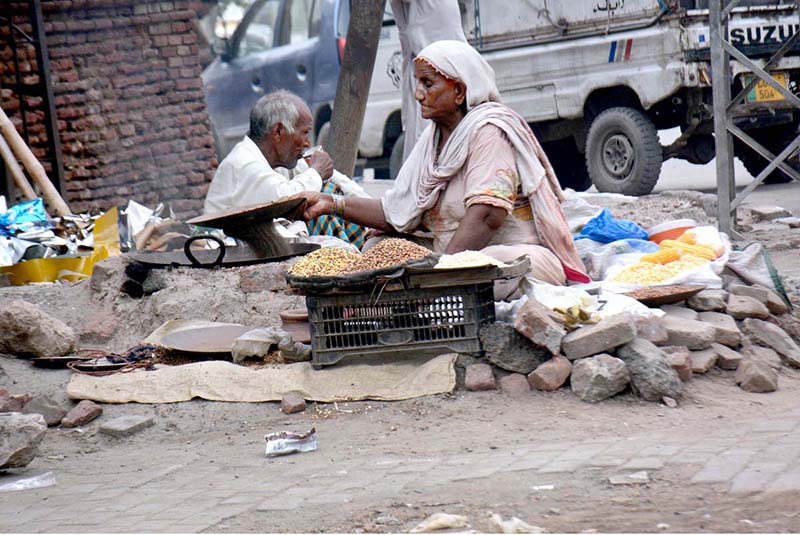 An elderly lady is cooking corn kernels near the Shahi Qila