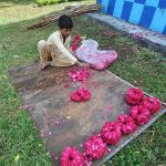 A young vendor busy in preparing flower garlands while sitting at roadside greenbelt in Federal Capital