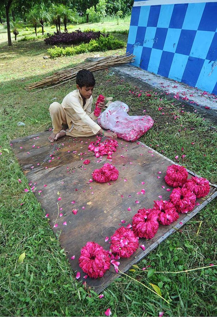 A young vendor busy in preparing flower garlands while sitting at roadside greenbelt in Federal Capital