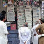 People are reading a newspaper displayed for sale by a shopkeeper at Abpara Market.