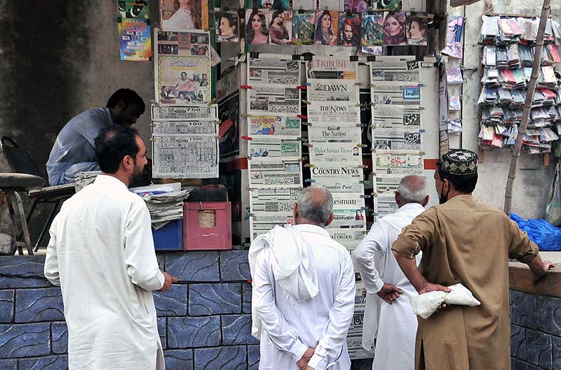 People are reading a newspaper displayed for sale by a shopkeeper at Abpara Market.