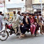 A significant group of individuals is traveling on tricycle carts along Railway Station Road