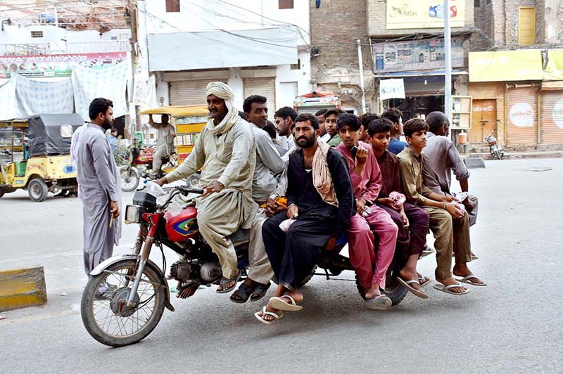 A significant group of individuals is traveling on tricycle carts along Railway Station Road