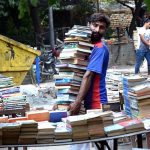 Customers are buying secondhand books from a roadside stall.
