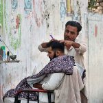 A street barber busy in hair cutting of a person at his roadside setup near Gulbahar Police Station