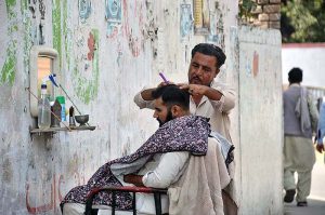 A street barber busy in hair cutting of a person at his roadside setup near Gulbahar Police Station