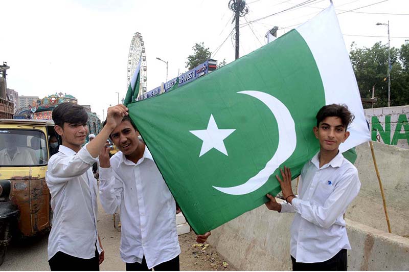 Youngsters are holding flags displayed by a vendor at the roadside, aiming to attract customers as the nation begins preparations to celebrate Independence Day with fitting celebrations