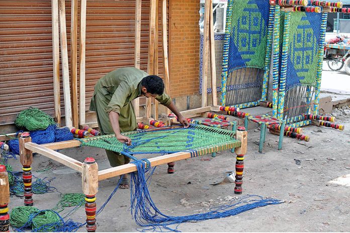 Workers knitting a traditional bed (Charpai) at his workplace.