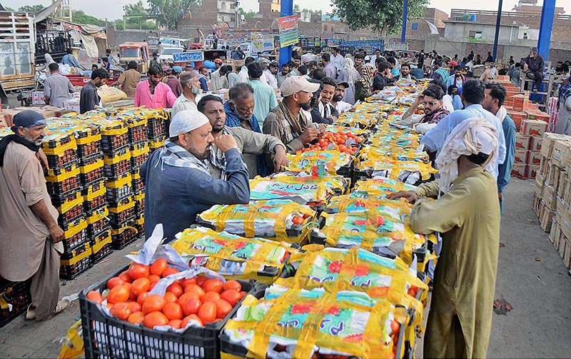 A vendor displaying tomatoes during an auction as shopkeepers participate in bidding at Vegetable Market