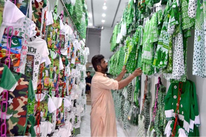 In anticipation of Pakistan's upcoming Independence Day celebrations, a shopkeeper proudly showcases children's suits adorned with Pakistani flags in his shop