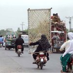 A woman holding a traditional Bed (charpai) while sitting rear seat of a Motorcycle