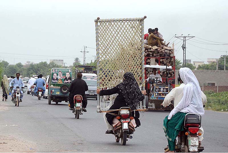 A woman holding a traditional Bed (charpai) while sitting rear seat of a Motorcycle