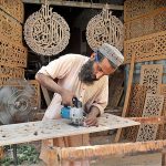 A carpenter busy in carving different designs on wooden sheet at his workplace