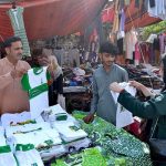 A woman is purchasing clothes adorned with the green and white flag of Pakistan, for her children to wear on the upcoming Independence Day