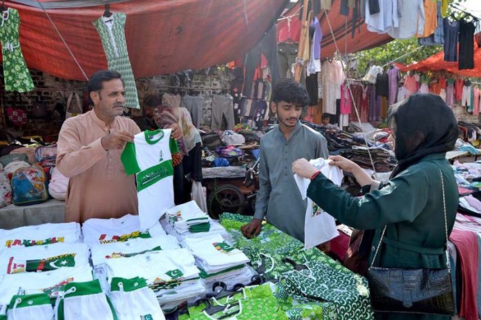 A woman is purchasing clothes adorned with the green and white flag of Pakistan, for her children to wear on the upcoming Independence Day