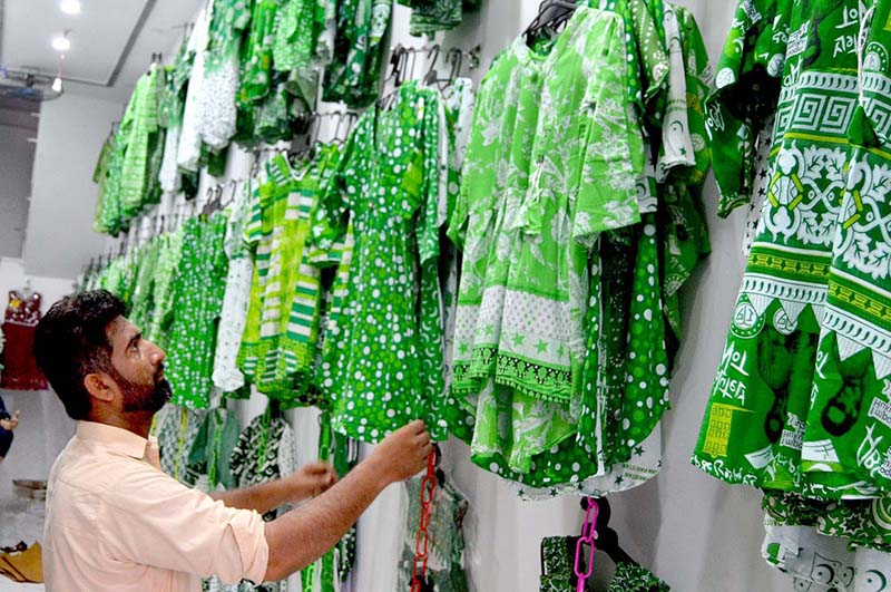 A woman is purchasing clothes adorned with the green and white flag of Pakistan, for her children to wear on the upcoming Independence Day