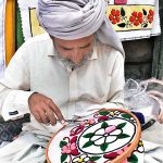 A skilled person making embroidery work on bed sheet and pillow to attract customers at his road side setup