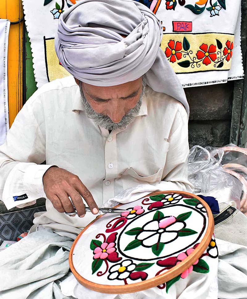 A skilled person making embroidery work on bed sheet and pillow to attract customers at his road side setup