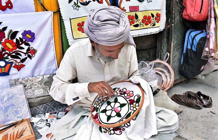 A skilled person making embroidery work on bed sheet and pillow to attract customer at his road side setup near NLI chowk A skilled person making embroidery work on bed sheet and pillow to attract customer at his road side setup near NLI chowk