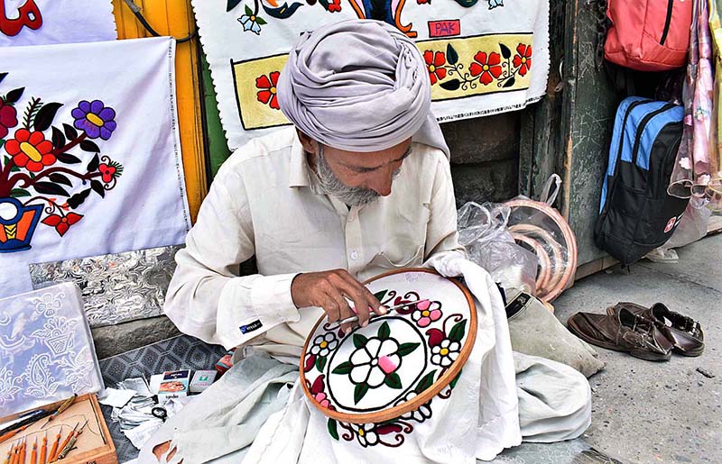 A skilled person making embroidery work on bed sheet and pillow to attract customer at his road side setup near NLI chowk