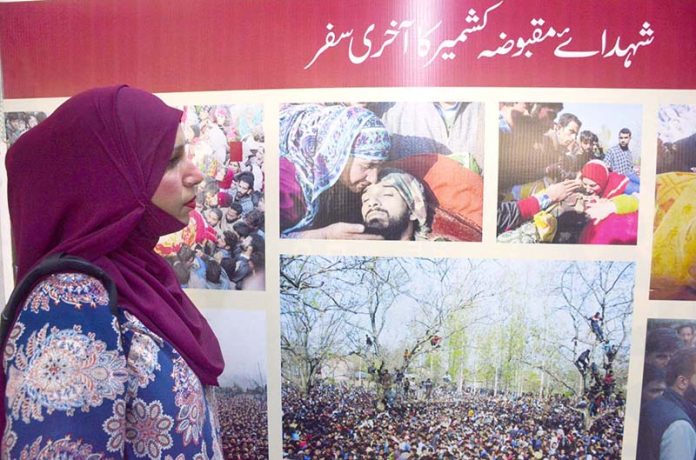 A girl looking at a picture put on display in a pictorial exhibition on 'Kashmir Exploitation Day' at Arts Council of Pakistan