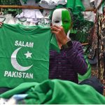 A vendor wear national flag colour face mask holds national flag for sell at his stall at paper market in connection with Pakistan's Independence Day celebrations