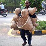 A street vendor displaying traditional handmade baskets while shuttling on the road.