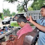 A young barber busy in cutting the hair of a customer at his roadside setup.