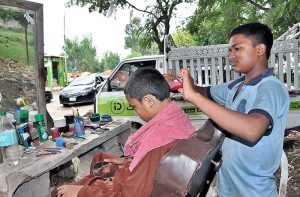  A young barber busy in cutting the hair of a customer at his roadside setup.