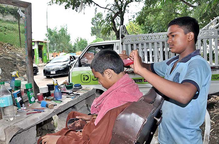 A young barber busy in cutting the hair of a customer at his roadside setup.