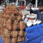 A vendor sprinkling water on coconut to keep them fresh at roadside in the Federal Capital.