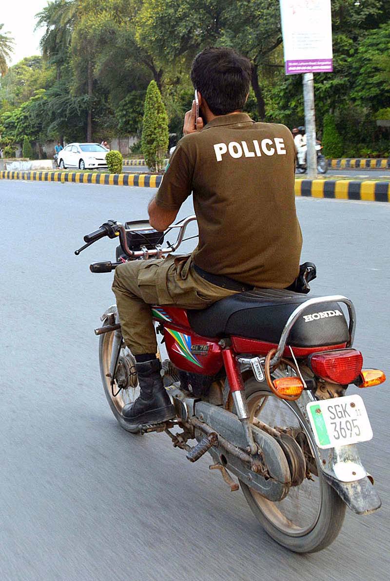 A police official on the way without wearing safety helmet and using mobile while driving motorcycle at College Road.