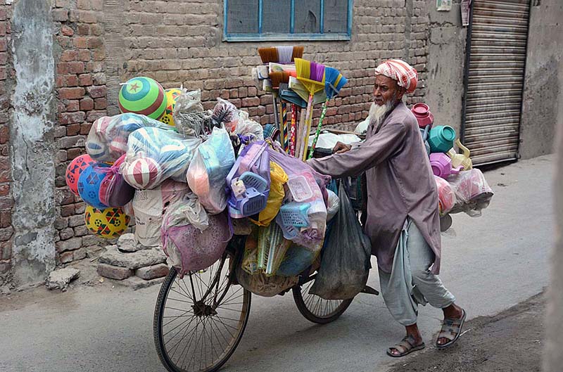 An elderly vendor along with bicycle loaded with household items for selling while shuttling in streets to earn livelihood.