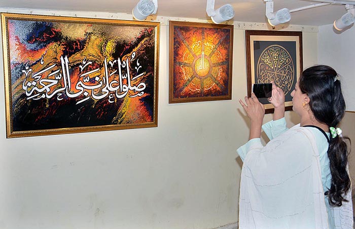Female visitor capture painting in mobile during Quranic calligraphy exhibition at Arts Council.