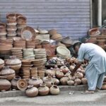 Vendor is busy arranging and displaying clay-made pots to attract customers at his roadside setup.