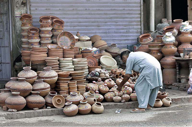 Vendor is busy arranging and displaying clay-made pots to attract customers at his roadside setup.
