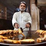 A vendor preparing fry fish at his shop for customers.