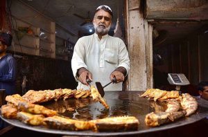 A vendor preparing fry fish at his shop for customers.