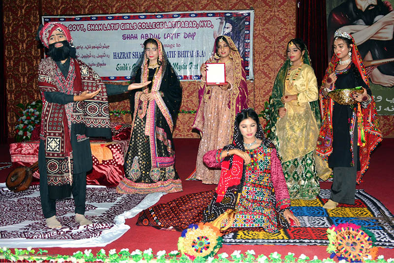 Female students performing tableau on stage at Shah Latif Girls College