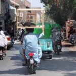 A person carrying a cage on his head while sitting on the rear seat of a motorcycle.