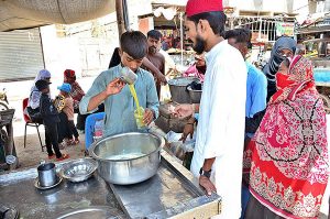People purchasing sugarcane juice from vendor at Latifabad during hot weather in the city.
